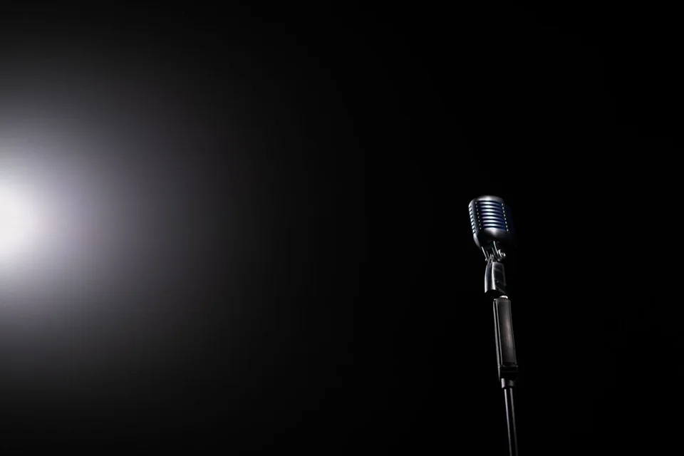 Imagem ilustrativa: microfone iluminado em um palco escuro, representando as aulas de canto.